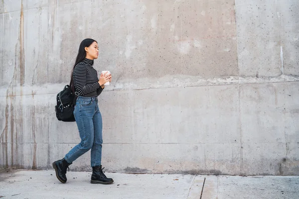 若いアジアの女性の肖像と灰色の壁に対するコーヒーカップを保持歩くと — ストック写真