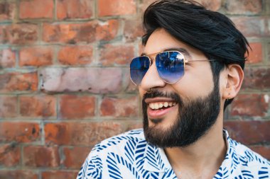 Tuğla duvara karşı yaz kıyafetleri ve güneş gözlüğü takan genç yakışıklı adamın portresi. Şehir konsepti.