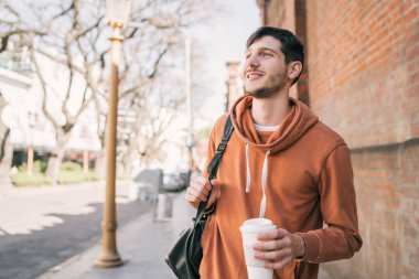 Sokakta yürüyen ve elinde bir fincan kahve tutan genç adamın portresi. Şehir konsepti.