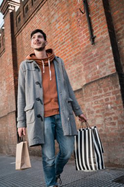 Sokakta yürürken alışveriş torbaları tutan yakışıklı bir adamın portresi. Kentsel, alışveriş konsepti.