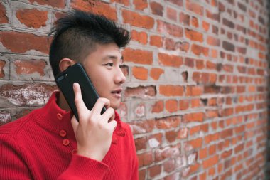 Dışarıda, duvarın karşısında telefonla konuşan Asyalı genç bir adamın portresi. İletişim konsepti.