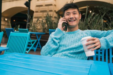 Bir kafede otururken telefonla konuşan Asyalı genç adamın portresi. İletişim konsepti.