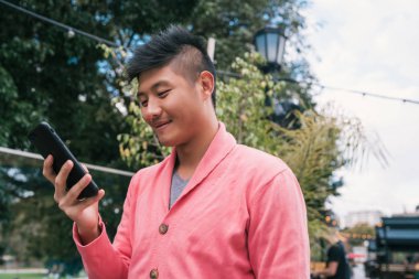 Sokakta cep telefonunu kullanan genç Asyalı adamın portresi. İletişim konsepti.