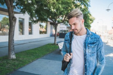 Omuzlarında sırt çantasıyla sokakta yürüyen çekici bir gencin portresi. Şehir konsepti.