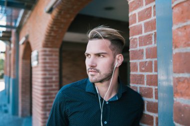 Sokakta kulaklıkla müzik dinleyen yakışıklı bir adamın portresi. Şehir konsepti.