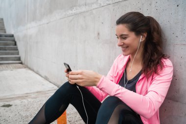 Atletik bir kadının portresi gri arka planda antremana ara vermek için cep telefonunu kullanıyor. Spor ve sağlık yaşam tarzı.