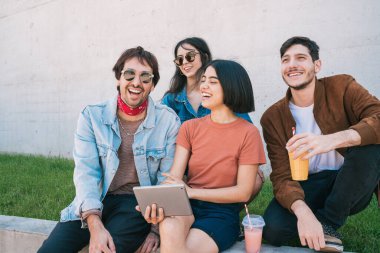 Bir grup arkadaşın dışarıda otururken birlikte eğlendikleri ve dijital tablet kullandıkları portre. Teknoloji, yaşam tarzı ve arkadaşlık kavramı.