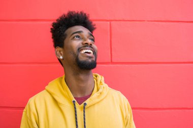 Genç Afro-Amerikan bir adamın portresi. Kendinden emin görünüyor ve kırmızı duvara karşı poz veriyor..