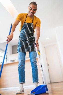Evde süpürgeyle yerleri süpüren Latin bir gencin portresi. Temizlik, ev işi ve temizlik konsepti.