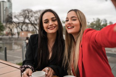 Kafede otururken selfie çeken iki genç arkadaşın portresi. Yaşam tarzı ve arkadaşlık kavramı.