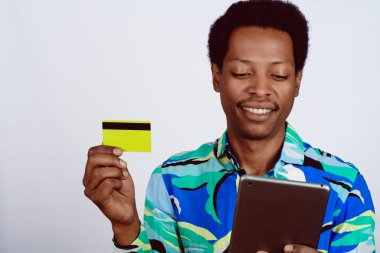 Kredi kartı tutan afro bir adamın portresi ve izole edilmiş arka planda dijital tablet kullanıyor. Çevrimiçi ve tüketici kavramı.