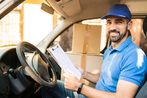 Portrait of a delivery man checking the delivery list while sitting in van. Delivery and shipping concept.