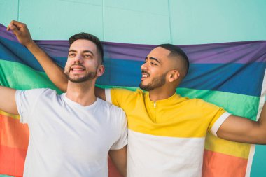 Sokakta gökkuşağı bayrağıyla sarılıp sevgilerini gösteren genç eşcinsel çiftin portresi. LGBT ve aşk konsepti