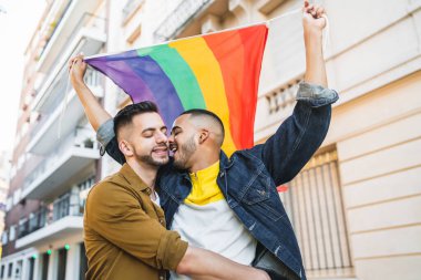 Sokakta gökkuşağı bayrağıyla kucaklaşan ve sevgilerini gösteren genç eşcinsel çiftin portresi. LGBT ve aşk konsepti