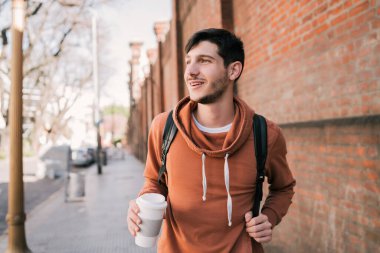 Sokakta yürüyen ve elinde bir fincan kahve tutan genç adamın portresi. Şehir konsepti.