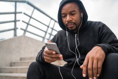 Beton merdivenlerde otururken cep telefonunu kullanan atletik bir adamın portresi. Spor ve sağlık konsepti.