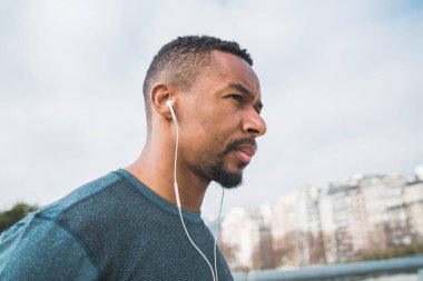 Açık havada egzersiz yaparken kulaklıkla müzik dinleyen atletik bir adamın portresi. Spor ve sağlıklı yaşam tarzı.