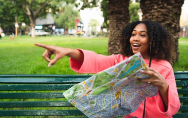 Elinde harita tutan ve bir yeri gösteren güzel Afro-Amerikan kadının portresi. Seyahat konsepti. Açık havada..