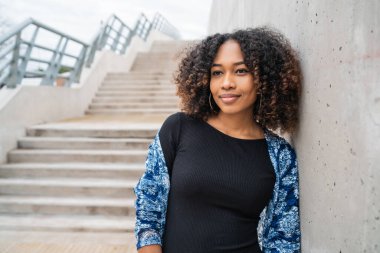 Dışarıdaki beton merdivenlerde duran kıvırcık saçlı güzel Afro-Amerikan kadının portresi.. 