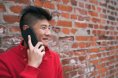 Dışarıda, duvarın karşısında telefonla konuşan Asyalı genç bir adamın portresi. İletişim konsepti.