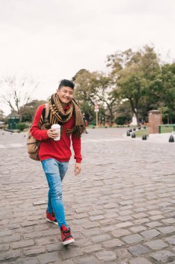 Sokakta yürürken bir fincan kahve içen genç Asyalı adamın portresi. Şehir konsepti.
