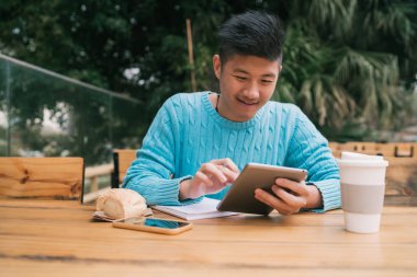 Bir kafede otururken dijital tabletle çalışan genç Asyalı adamın portresi. Teknoloji konsepti.