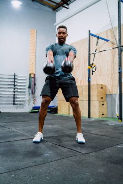 Spor salonunda çaydanlıkla egzersiz yapan genç bir sporcunun portresi. Crossfit, spor ve sağlıklı yaşam tarzı konsepti.