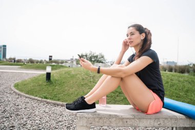 Eğitime ara verdiğinde cep telefonunu kullanan atletik bir kadının portresi. Spor ve sağlık yaşam tarzı.