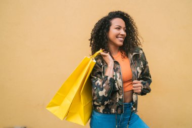 Sarı arka planda alışveriş torbaları tutan genç Afro-Amerikan Latin kadın portresi. Dükkan ve yaşam tarzı konsepti.
