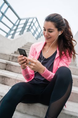 Eğitime ara verdiğinde cep telefonunu kullanan atletik bir kadının portresi. Spor ve sağlık yaşam tarzı.