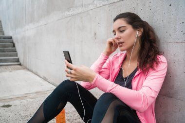 Atletik bir kadının portresi gri arka planda antremana ara vermek için cep telefonunu kullanıyor. Spor ve sağlık yaşam tarzı.