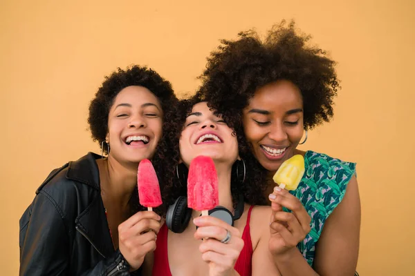 Portrait of multi-ethnic group of friends having fun and enjoying summertime while eating ice cream against yellow background.
