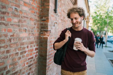 Sokakta yürüyen ve elinde bir fincan kahve tutan genç adamın portresi. Şehir konsepti.