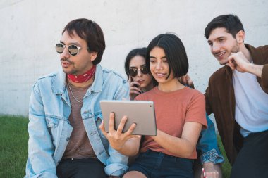 Bir grup arkadaşın dışarıda otururken birlikte eğlendikleri ve dijital tablet kullandıkları portre. Teknoloji, yaşam tarzı ve arkadaşlık kavramı.