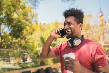Dışarıda kahve içerken telefonla konuşan genç afro adamın portresi. İletişim, yaşam tarzı ve kentsel konsept.