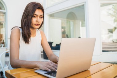 Bir kafede otururken dizüstü bilgisayarını kullanan genç Latin kadının portresi. Teknoloji ve yaşam tarzı kavramı.