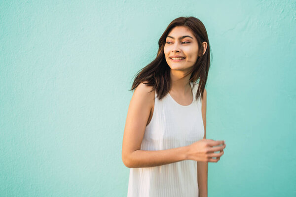 Portrait of young latin woman smiling and standing on light blue background. Urban concept.