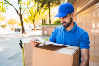 Karton kutular taşıyan bir teslimatçının portresi ve açık havada kontrol listesi. Teslimat ve nakliye konsepti.