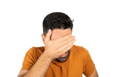 Stüdyodaki beyaz arka planda korkmuş ve yüzünü kapatmış genç bir adamın portresi..