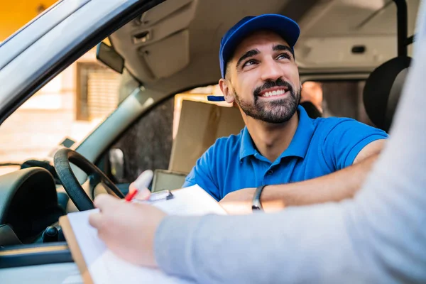 Portrait of a delivery man in van while customer putting signature in clipboard. Delivery and shipping concept.
