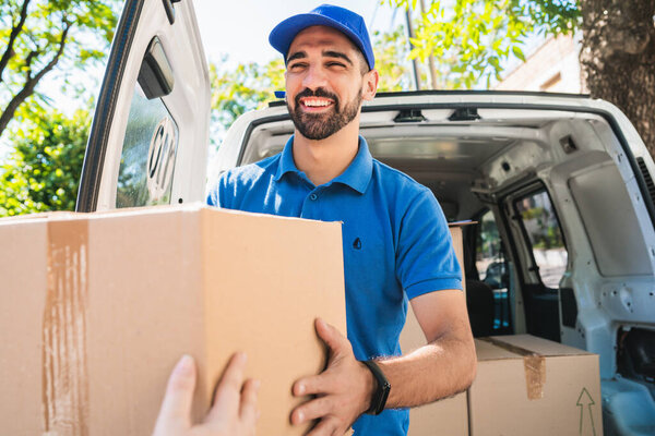 Portrait of a delivery man carrying packages while making home delivery to his customer. Delivery and shipping concept.