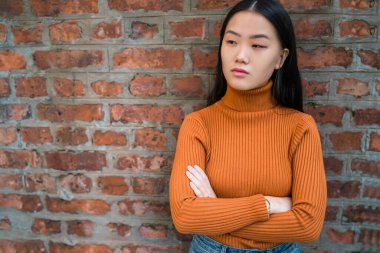 Kendine güvenen ve tuğla duvar arkasında duran genç, güzel Asyalı bir kadına yakından bakın..