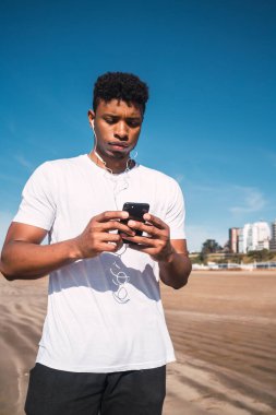 Sahilde antremana ara verdiğinde cep telefonunu kullanan bir atletin portresi. Spor ve sağlık yaşam tarzı.