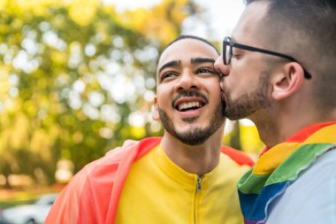Genç eşcinsel çiftin portresi. Sokakta gökkuşağı bayrağıyla kucaklaşıp sevgilerini gösteriyorlar. LGBT ve aşk konsepti