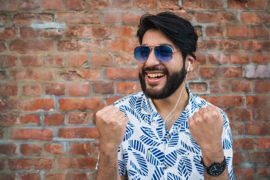 Yazlık kıyafetler giyen ve tuğla duvara karşı zaferi kutlayan genç yakışıklı bir adam. Kentsel ve başarı kavramı.