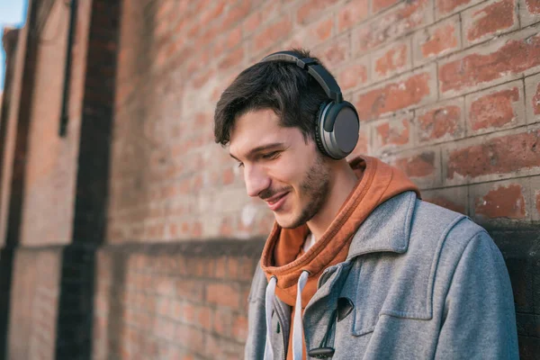 stock image Portrait of young latin man listening to music with headphones against brick wall. Urban concept.