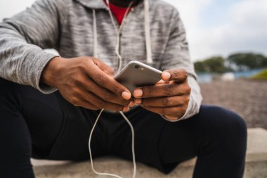 Açık havada otururken cep telefonuyla antrenman yapan bir sporcunun portresi. Spor ve sağlık yaşam tarzı.