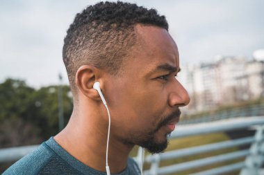 Açık havada egzersiz yaparken kulaklıkla müzik dinleyen atletik bir adamın portresi. Spor ve sağlıklı yaşam tarzı.