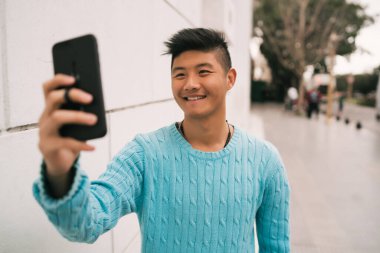 Sokakta dikilirken cep telefonuyla selfie çeken Asyalı genç adamın portresi.. 