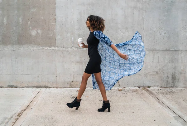 若いアフロ系アメリカ人女性がコーヒーを飲みながら歩いている姿が描かれている — ストック写真